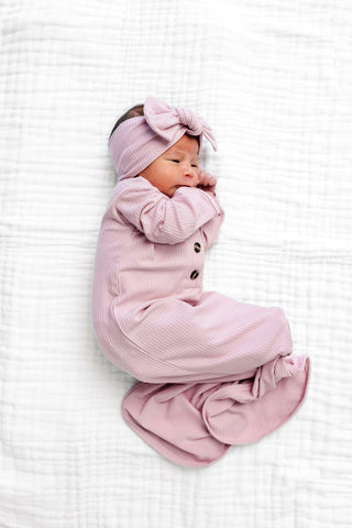 Lou Lou and Company Ribbed Knotted Gown - Haven
Newborn baby in a pink outfit with a matching headband on a white textured blanket