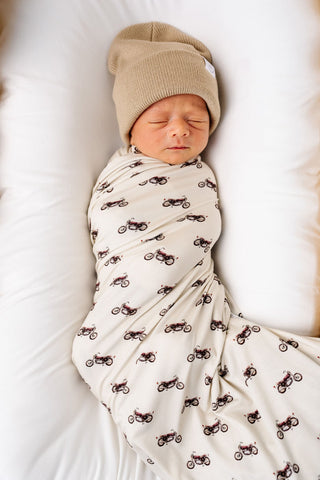 Lou Lou and Company Swaddle Blanket - Cruz
Newborn baby swaddled in a blanket with motorcycle patterns, wearing a beige hat.