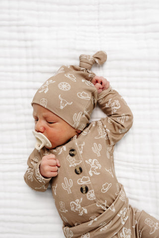 Lou Lou and Company Top Knot Hat - Wyatt
Newborn baby wearing a beige outfit with white patterns on a white background
