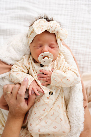 Lou Lou and Company Knotted Gown - Annie
Newborn baby wrapped in a white blanket with a pacifier, held by a person.