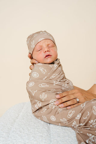 Lou Lou and Company Swaddle Blanket - Wyatt
Newborn baby swaddled in a patterned blanket with a matching hat, held by a person against a plain background.