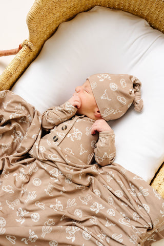 Lou Lou and Company Top Knot Hat - Wyatt
Newborn baby in a beige outfit with patterns, lying in a woven basket.