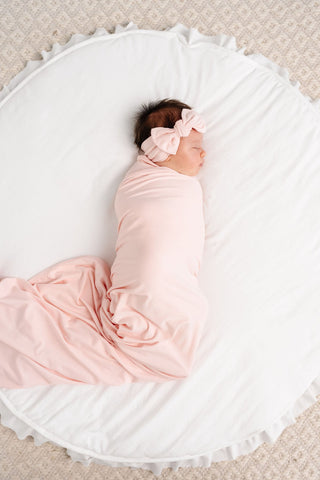 Lou Lou and Company Headband - Sophie
Newborn baby wrapped in pink swaddle with matching headband on a white circular bed.