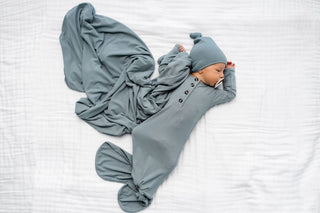 Lou Lou and Company Ribbed Knotted Gown - Ford
Baby wrapped in a gray swaddle with matching hat on a white blanket