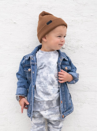 Little Bipsy Chunky Knit Beanie - Chestnut
Child wearing a denim jacket, tie-dye shirt, and camouflage pants against a white textured wall.