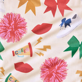 Posh Peanut Sabrina Criss-Cross Twirl Dress Colorful fabric pattern with pom-poms, lips, and a megaphone on a white background