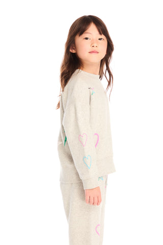 Chaser Winter Love Stitches Long Sleeve
Young girl wearing a light gray sweatshirt with colorful heart designs on a white background