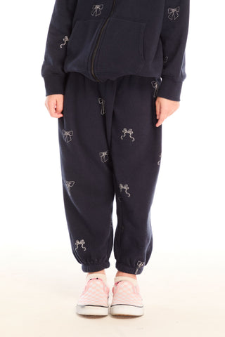 Chaser Tossed Glitter Bows Pants
Person wearing a navy tracksuit with small white graphics on a white background
