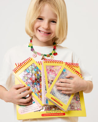 Super Smalls Make It Sweet Gemify™ Sticker Booklet Child holding two sticker books with colorful stickers on a white background