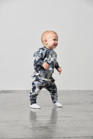 Little Bipsy Marble Pullover - Blue
Baby in a tie-dye outfit standing on a gray floor with a white wall background