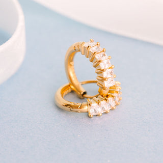 Pierced Co. Diamond Ring Huggies
Gold ring with clear gemstones on a light blue surface