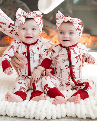 In My Jammers Merry Little Bows Zipper Romper
Two babies in matching red and white outfits with bow headbands, sitting on a white surface.