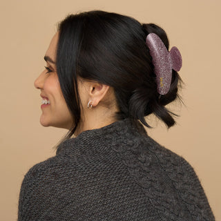 Kitsch Holiday Pink Glitter Claw Clip
Woman with a purple hair accessory in her bun against a beige background