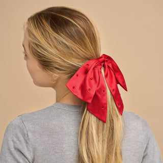 Kitsch Holiday Satin & Rhinestone Bow Scrunchie
 Woman with a red hair bow in her blonde hair against a beige background
