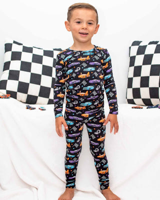Lev Baby Pajama Set - Elias
Child wearing a colorful car-patterned pajama set on a white background with checkered pillows.