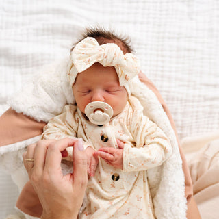 Lou Lou and Company Headband - Annie
Newborn baby wearing a white outfit and headband, holding a pacifier, with a soft white blanket in the background.