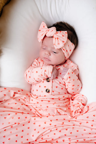 Lou Lou and Company Headband - Miley
Baby in a pink outfit with heart patterns and large bows on a white background
