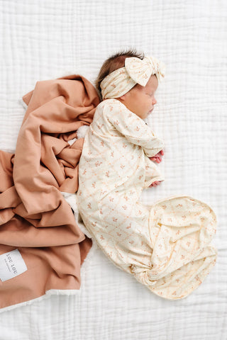 Lou Lou and Company Knotted Gown - Annie
Newborn baby wrapped in a swaddle with a pink blanket on a textured white surface