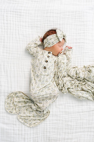 Lou Lou and Company Knotted Gown - Etta
Newborn baby wrapped in a floral patterned swaddle on a white textured surface