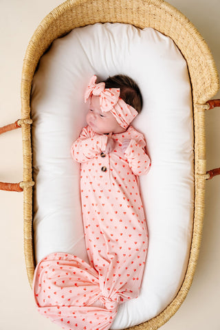 Lou Lou and Company Knotted Gown - Miley
Newborn baby in a pink outfit with a bow in a moses basket.