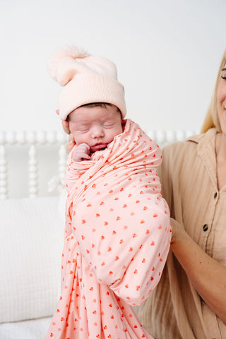 Lou Lou and Company Swaddle Blanket - Miley
Newborn baby wrapped in a pink blanket with red hearts, wearing a matching pink hat, held by a person against a white background.