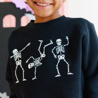 Sweet Wink Silly Skelly Glow In The Dark Halloween Sweatshirt - Black Child wearing a black sweatshirt with skeleton designs on a plain background