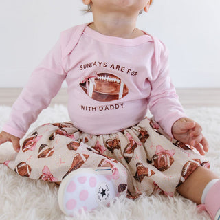 Sweet Wink Football With Daddy Long Sleeve Bodysuit - Ballet Child wearing a pink shirt with text and a skirt with football patterns on a white background