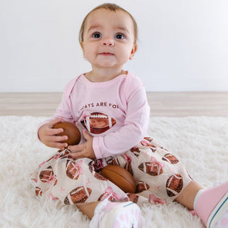 Sweet Wink Football With Daddy Long Sleeve Bodysuit - Ballet Baby in pink outfit with football design holding a brown ball on a white surface