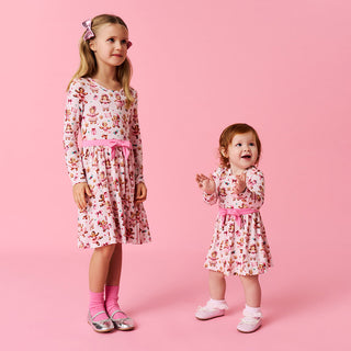 Posh Peanut Bow Twirl Bodysuit Dress- Ginger Posh
Two young girls wearing matching floral dresses on a pink background
