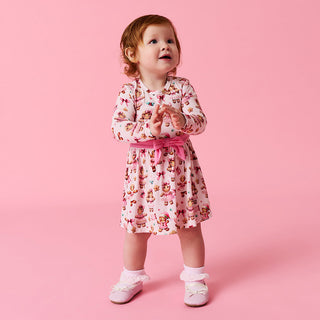 Posh Peanut Bow Twirl Bodysuit Dress- Ginger Posh
Child wearing a patterned dress with a pink belt on a pink background
