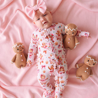 Posh Peanut Ruffled Zippered Footie - Ginger Posh
Baby in a pink outfit with gingerbread-themed toys on a pink blanket