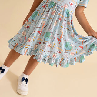 Posh Peanut Steve Ruffled Twirl Dress Child wearing a patterned dress with a beige background