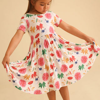 Posh Peanut Sabrina Criss-Cross Twirl Dress Young girl wearing a colorful floral dress against a beige background