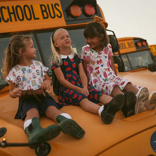 Posh Peanut Lilian Collared Twirl Dress Three children sitting on the hood of a yellow school bus.
