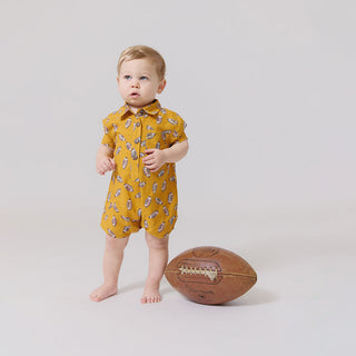 Blue Rooster Baby Boys Easton Jumper - Flying Footballs Baby in a yellow romper with a pattern, standing next to a football on a plain background