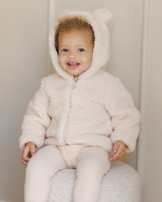 Quincy Mae Bear Jacket - Antique
Child wearing a fluffy white jacket with bear ears sitting on a chair.