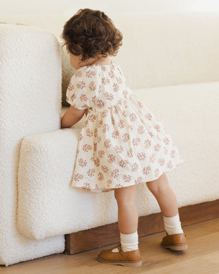 Quincy Mae Bella Dress - Daylily 
Child in a floral dress standing next to a white couch