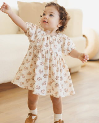 Quincy Mae Bella Dress - Daylily 
Child wearing a floral dress standing indoors with a neutral background