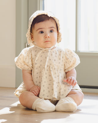 Quincy Mae Francy Set - Bluebell 
Baby wearing a floral dress and bonnet sitting on a wooden floor.