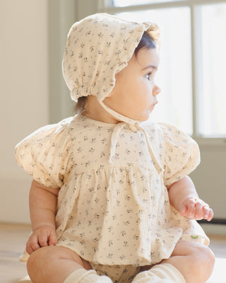 Quincy Mae Francy Set - Bluebell 
Baby wearing a floral bonnet and romper sitting indoors.