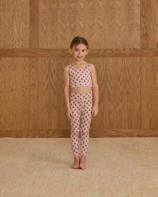 Play by Rylee & Cru Swift Sports Bra - Blush Fleur Play by Rylee & Cru Basic Legging - Blush Fleur Young girl wearing a matching top and pants set with a floral pattern against a wooden wall.