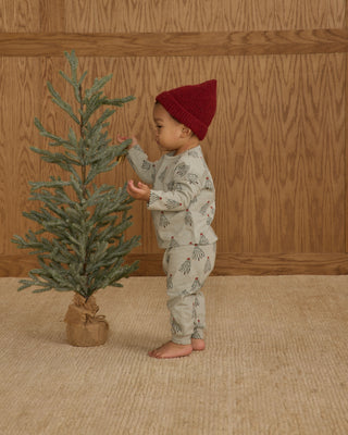 Rylee & Cru Long Sleeve Tee + Pant Set - Trees
Child in pajamas and red hat standing next to a small Christmas tree against a wooden wall.