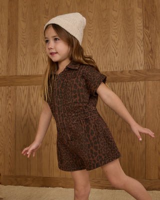 Rylee & Cru Utility Romper - Leopard
Young girl in a leopard print dress and cream beanie standing against a wooden paneled wall.