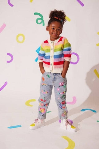 Lola and The Boys Rainbow Bright Knit Cardigan Child wearing a colorful striped sweater and patterned pants against a light background with colorful shapes.