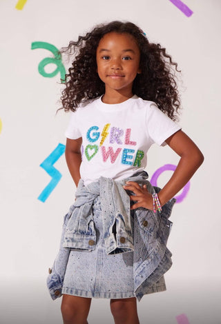 Lola and The Boys Rainbow Sparkle Denim Skirt
Young girl wearing a white t-shirt with colorful text, standing against a light background.