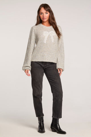 Saltwater Luxe Long Sleeve Bow Sweater in Heather Grey
Woman wearing a patterned sweater and black jeans on a plain background