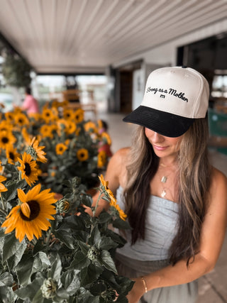 Strong As A Mother® Script Canvas Hat - Natural / Black
Woman wearing a cap with text, standing among sunflowers indoors.