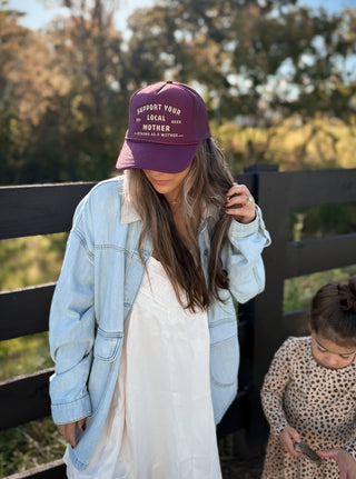 Support Your Local Mother® Trucker Hat - Burgundy
Woman wearing a purple cap with text, standing outdoors with a child.