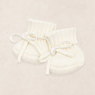 Lou Lou and Company Knit Booties - Ivory
Pair of white knitted baby booties with bows on a beige background