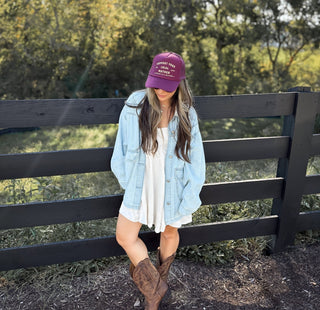 Support Your Local Mother® Trucker Hat - Burgundy
Woman wearing a purple cap and light blue jacket standing in front of a wooden fence with greenery in the background.
